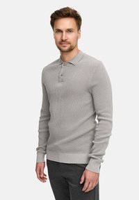 Pullover a coste grigio chiaro con colletto polo, tre bottoni e polsini aderenti, abbinato a pantaloni grigio scuro.