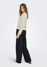 Pull crème avec rayures noires, poignets et ourlet côtelés ; associé à un pantalon noir à jambes larges et taille haute. Texture lisse et coupe décontractée.
