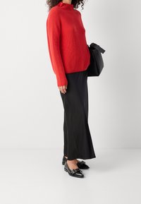 Rode geribde gebreide trui met een hoge halslijn, gecombineerd met een zwarte satijnen rok en zwarte ballerina's met decoratieve hardware accenten.