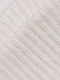 Fehér kötött anyag, texturált bordás mintával, jellegzetes vízszintes vonalakkal és puha, dundi megjelenéssel.