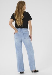 Ljusblå högmidjade jeans med raka ben, två bakfickor, kontrasterande sömmar, i kombination med en svart kortärmad skjorta och svarta klackar.