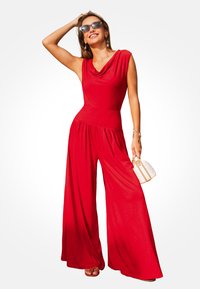 Mono rojo de pierna ancha con escote drapeado y cintura ajustada. Fabricado con un tejido suave; acompañado de un pequeño bolso blanco.
