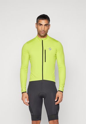 Langarm-Radjacke in leuchtendem Limettengrün, mit durchgehendem Reißverschluss vorne und tailliertem Design, kombiniert mit schwarzen Radhosen.