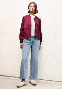 Veste bomber en satin bordeaux, t-shirt blanc à col rond, jeans menthe large en bleu clair et baskets grises avec des accents marron. Textures lisses partout.