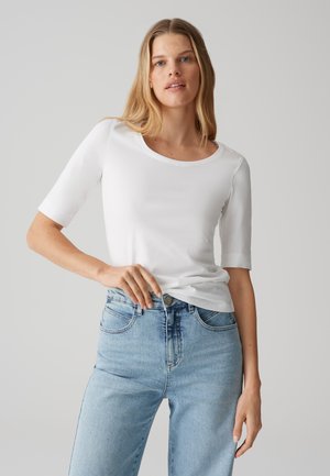 White short-sleeve top with a round neckline, made of smooth fabric. Paired with mid-rise light blue jeans, featuring a classic fit.