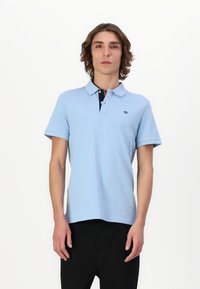 Lyseblå polo skjorte med svart krage, korte ermer, liten logo på brystet, og en glatt tekstur.
