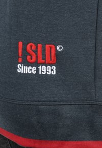 Mørkegrå sweatshirt med rødt og hvidt broderet logo "! SLD" med "Since 1993" nedenfor. Ribbede manchetter og kant. Blød tekstur.