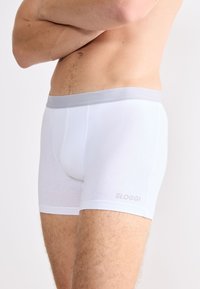Boxer in cotone bianco con un elastico grigio in vita. Presentano una texture liscia e un sottile logo Sloggi sul lato inferiore.