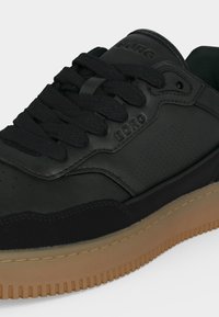 Baskets en cuir noir avec une semelle épaisse en caoutchouc marron, des lacets noirs et "BORG" embossé sur le côté et la languette.
