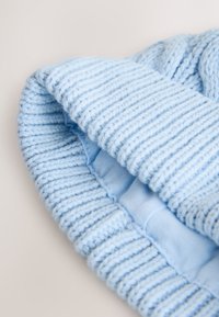 Lichtblauwe gebreide muts met een geribbelde structuur. De binnenkant heeft een gladde, lichtblauwe voering. De stof lijkt zacht en flexibel.