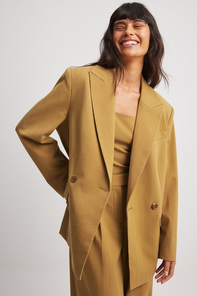 Blazer croisé en tissu jaune moutarde. Il présente des revers larges, de gros boutons et une coupe décontractée avec des épaules accentuées.