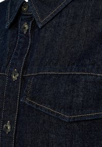 Jeans košulja u tamnoplavoj nijansi, s kontrastnim šavovima, klasičnom kragnom, prednjim džepom i dugmadima s okruglim, tamnim dugmadima.