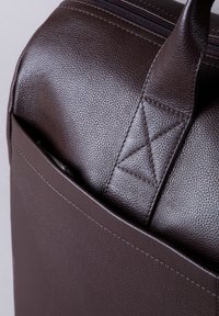 Brown leather bag with a textured surface, featuring a zip closure, prominent stitching details, and a triangular accent on the handle.
