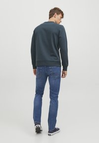 Felpa navy con scollatura rotonda e polsini a coste abbinata a jeans blu con cuciture sui taschini posteriori e scarpe stile sneaker.