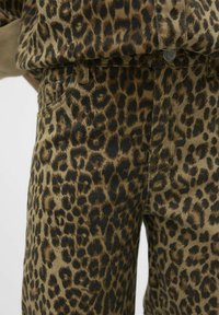 Tkanina s leopardjim vzorom v odtenkih rjave in črne barve z teksturirano površino. Vključuje jeans z žepi in gumbom za zapiranje.