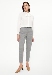 Blusa blanca con detalle de lazo; pantalones tapered de cuadros grises con acentos azules; modelo llevando tacones de punta beige.