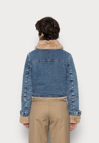 Chaqueta de mezclilla con un diseño recortado, cuello y puños de piel sintética, con un lavado azul y acentos en contraste de color marrón claro.
