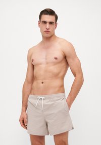 Shorts de bain beiges avec un tissu texturé, taille élastique et cordon blanc, comportant des poches latérales et longueur mi-cuisse.