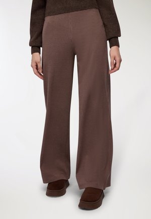 Pantaloni ampi marroni con un motivo a quadri testurizzato, realizzati in un materiale morbido. Abbinati a scarpe con piattaforma marroni scure.