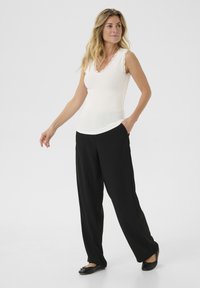 Weißes ärmelloses Tanktop mit Spitzenbesatz am Ausschnitt, kombiniert mit lockeren schwarzen Hosen und flachen schwarzen Schuhen. Einfaches, elegantes Design.