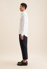 Wit en blauw gestreept overhemd met knopen, donkere broek en zwarte schoenen. Slim fit met lange mouwen en een getailleerde pasvorm.