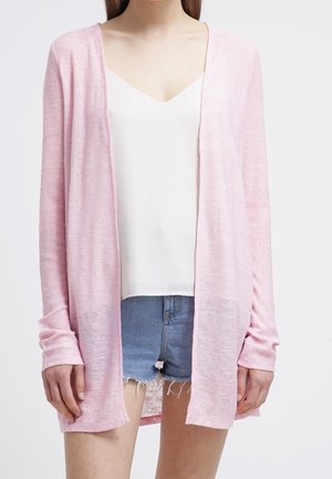 Lettet, åben-front cardigan i lys pink. Lange ærmer, blød tekstur og en afslappet pasform. Kombineret med en hvid top og denimshorts.