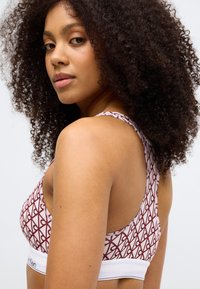 Branded bralette featuring a geometric red and white pattern, seamless design, wide straps, and a white elastic band with logo.