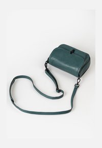 Borsa a tracolla in pelle verde acqua con forma arrotondata, tracolla regolabile, apertura superiore con zip e dettagli in hardware nero. Texture liscia con cuciture sottili.