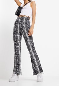 Pantaloni a vita alta, svasati, in stampa serpente bianca e nera, realizzati in materiale lucido. Abbinati a un crop top bianco e sneakers bianche.