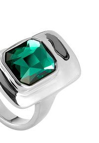 Anillo de plata con una gran gema verde facetada, montada en una sleek banda de metal pulido con curvas suaves y diseño geométrico.