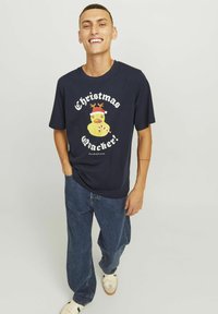 Mørkeblå bomulds t-shirt med grafik af en gul and iført rensdyrhorn, med teksten "Christmas Quacker!" i hvidt og rødt.