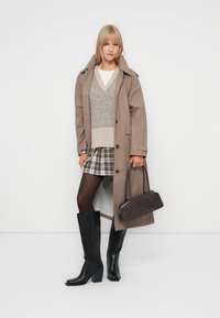 Brown trench coat over a grey sweater with a v-neck, plaid mini skirt, black knee-high boots, and a small brown handbag.