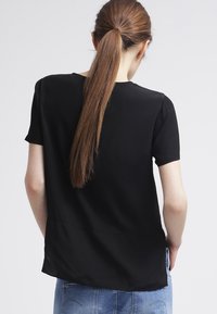 Svart kortärmad blus med avslappnad passform, slät textur och subtil detalj med söm på baksidan. Matchad med blå denimjeans.