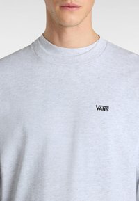 Šedá mikina s kulatým výstřihem vyrobená z měkké bavlněné směsi, s malým černým logem "VANS" na levé straně hrudi. Hladká textura, bez vzorů.