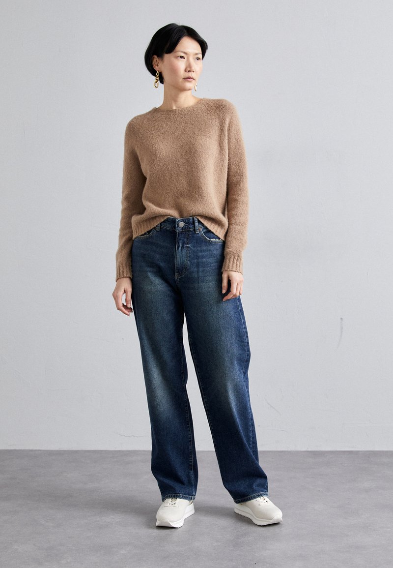 Light brown, fluffy sweater paired with blue wide-leg jeans and white sneakers. Accessories include gold earrings. Simple, relaxed fit design.