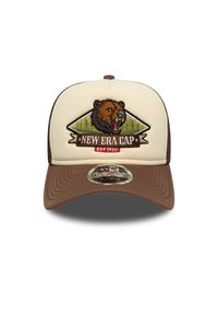 Καφέ και κρεμ καπέλο με έμβλημα αρκούδας, κεντημένο σχέδιο βουνού και πανό με τη φράση "NEW ERA CAP EST 1920". Το γείσο είναι καμπυλωτό.