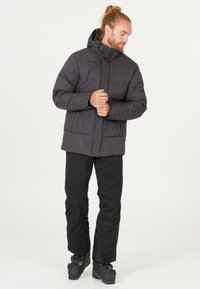 Herrarnas pufferjacka har en mörkgrå färg, quiltad design, hög krage med huva och framdraget blixtlås. Svarta byxor med förstärkta knän.