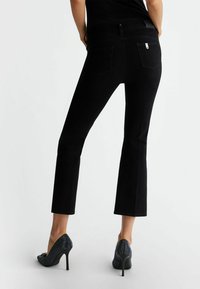 Jeans a zampa d'elefante in denim nero con vita media, dotati di due tasche posteriori e una texture elegante, abbinati a scarpe con tacco alto e brillanti.