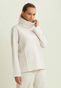Maglione a collo alto beige chiaro con una vestibilità comoda, maniche lunghe e pannelli laterali. Tessuto morbido e design minimalista.