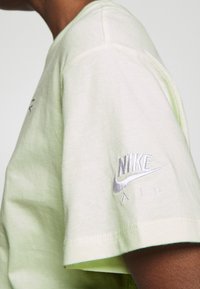 Light green cotton t-shirt featuring a crew neckline and short sleeves. Embroidered "NIKE AIR" logo in silver on the left sleeve.
