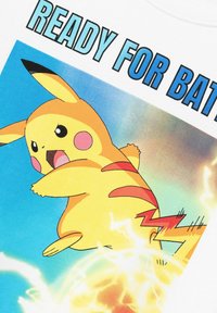 Balts T-krekls ar dzīvīgu Pikachu ilustrāciju, kuram ir rozā vaigi, sarkanas svītras un elektriskās dzirksteles uz zilas fona.