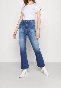 Blå jeans med hög midja och utsvängda ben, tillverkade i denim med en blekt tvätt, fem fickor och knäppning med knapp, kombinerade med en figurnära vit t-shirt.