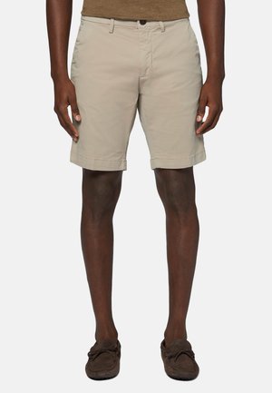 Beige shorts lavet af let materiale, med flad front, sidelommer og oprullede manchetter. Båret med mørkebrune slip-on sko.