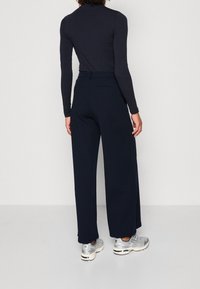 Marinblå vida byxor i mjukt tyg med hög midja, två bakfickor och kombinerade med silverfärgade sportskor.