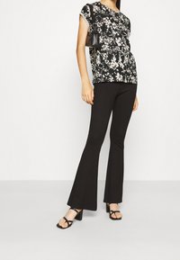 Květinový černobílý top s krátkým rukávem v kombinaci s černými rozšířenými kalhotami a černými sandály na blokovém podpatku. Malá černá kabelka. Hladká textura.