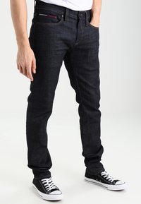Mörkblå denimjeans med slim fit, med klassisk femficksdesign, kontrasterande orangea sömmar och dragkedjestängning.