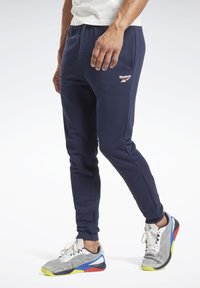 Marineblå sweatpants med en slim fit, snoretræk i taljen og Reebok-logo på låret; parret med multicolor sportssko.