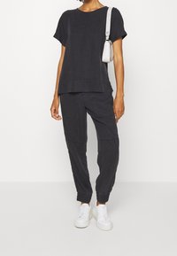 Sort bomuld T-shirt med korte ærmer og lagdelt design. Matcher med sorte joggers med elastiske manchetter. Hvide sneakers og en lille håndtaske.