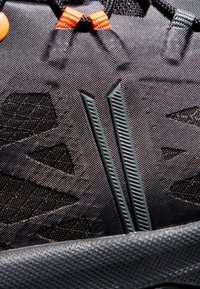 Schwarze Sportlederschuhe mit strukturiertem Obermaterial, orangefarbigen Akzenten und einem flexiblen Schnürsystem mit zwei unterschiedlichen, geformten Riemen.