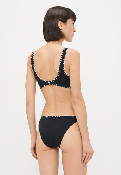 Juodas bikinis su plačiomis petnešomis, su baltais siuvinėjimo akcentais palei kraštus, užsegamas nugarinėje pusėje ir minimalistinio dizaino.